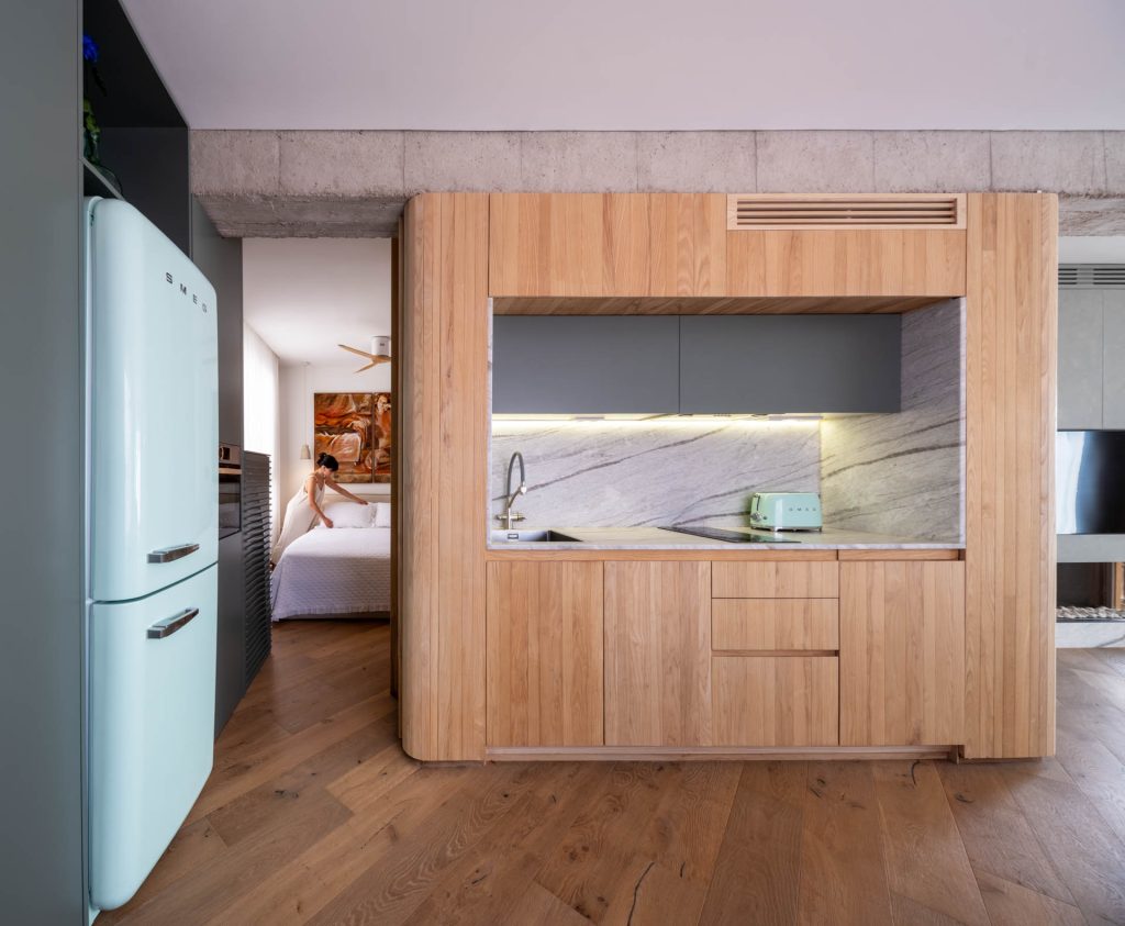 `Volumen de madera de la cocina con encimera de mármol en el Ático de hormigón y madera, reforma de Nítida arquitectos en Murcia, con hormigón visto en techo y apertura visual al dormitorio`