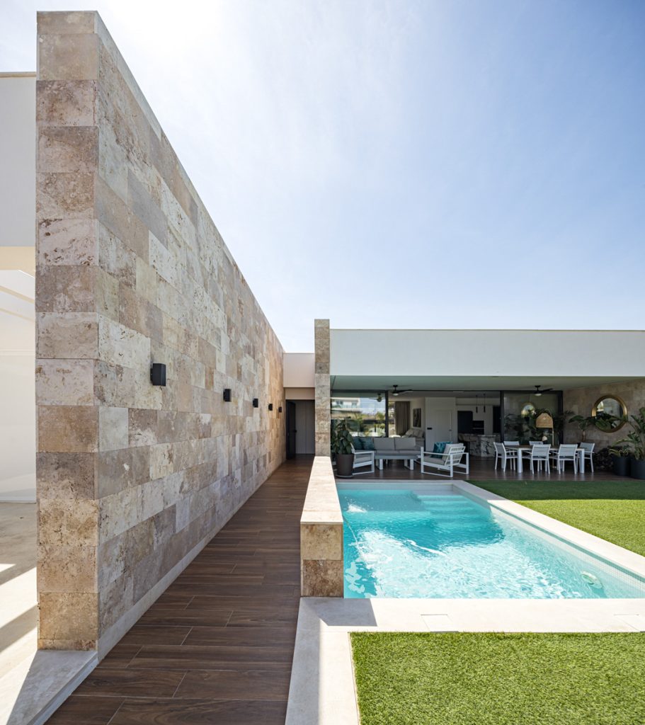 Exterior de Casa Macadán con piscina y jardín de césped, vivienda de muros de piedra y cubierta blanca · Arquitectura Nítida