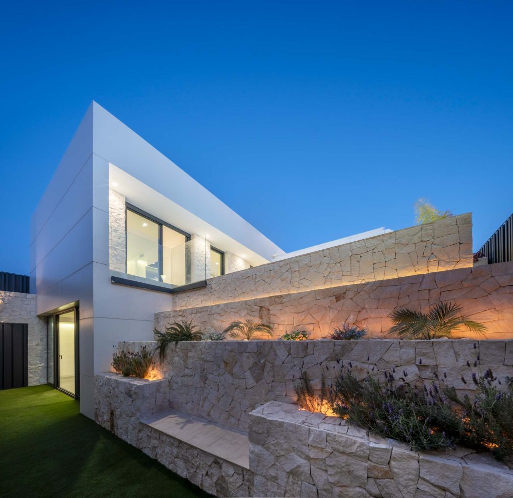 Fachada exterior de piedra de Casa Poniente iluminada con luces LED, diseño minimalista · Arquitectura Nítida