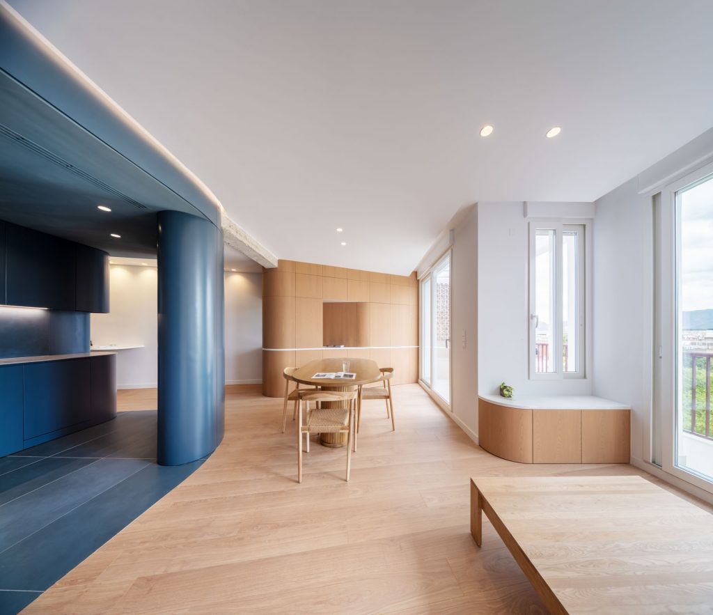 `Zona de comedor del Ático Azul Egeo con volumen curvo lacado en azul egeo, carpintería de madera y planta abierta sin particiones, reforma de Nítida arquitectos en Murcia`